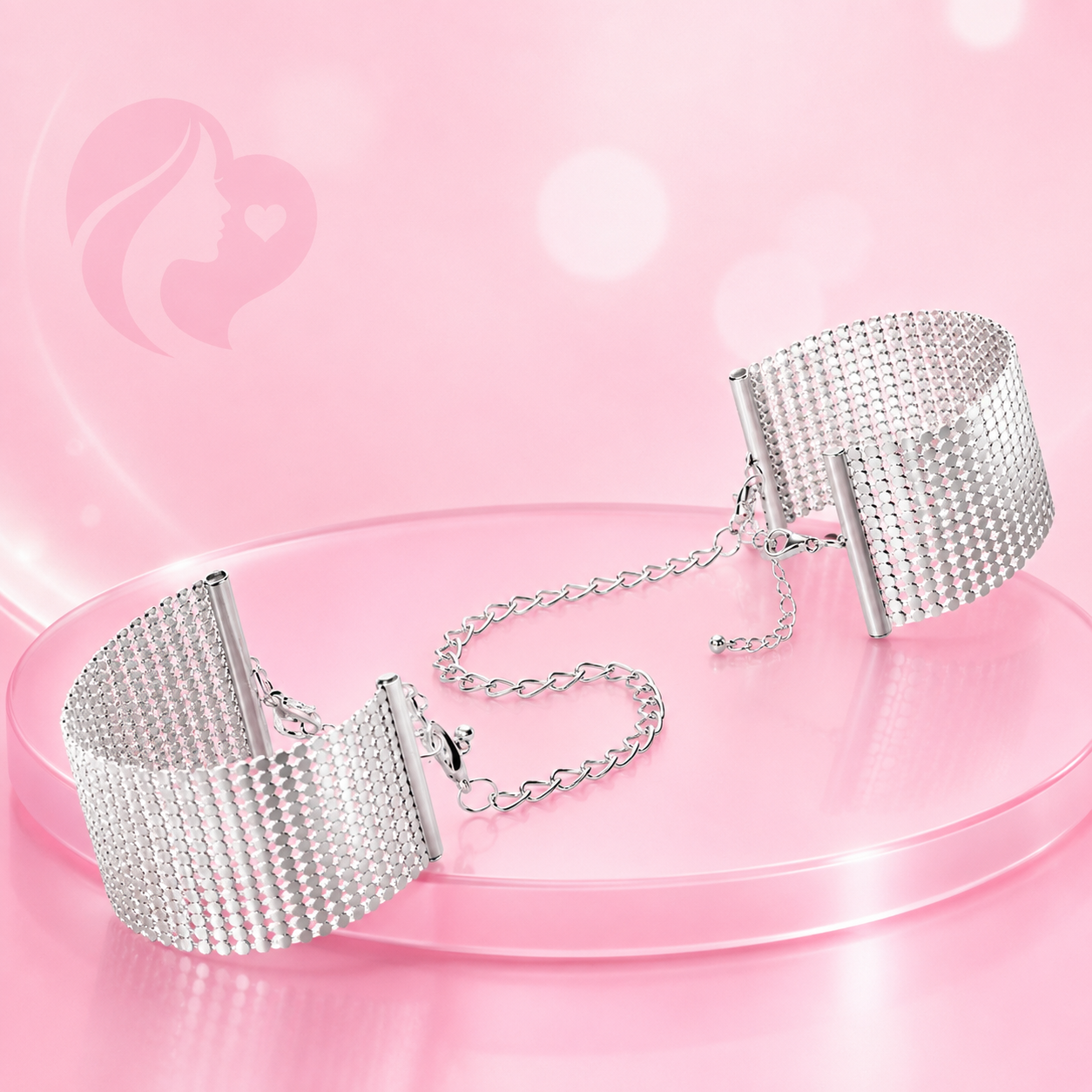Handschellen aus Metall mit Strass-Besatz und Metallkette, silberfarben, auf rosa Oberfläche präsentiert